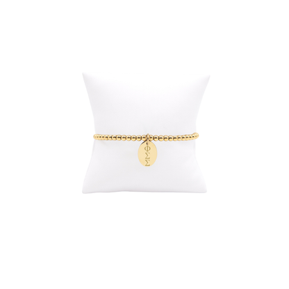 Phi Sigma Sigma gold beaded bracelet with small oval charm displayed on white pillow front view with vertical/stacked greek letters