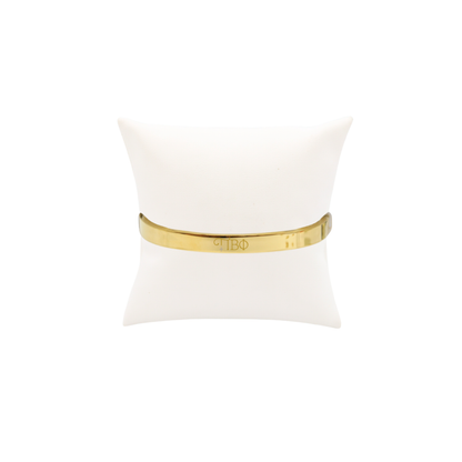Pi Beta Phi gold bangle bracelet displayed on white pillow front view with new horizontal greek letters