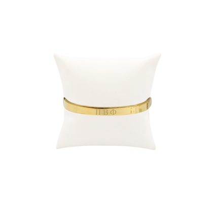 Pi Beta Phi gold bangle bracelet displayed on white pillow front view with horizontal greek letters