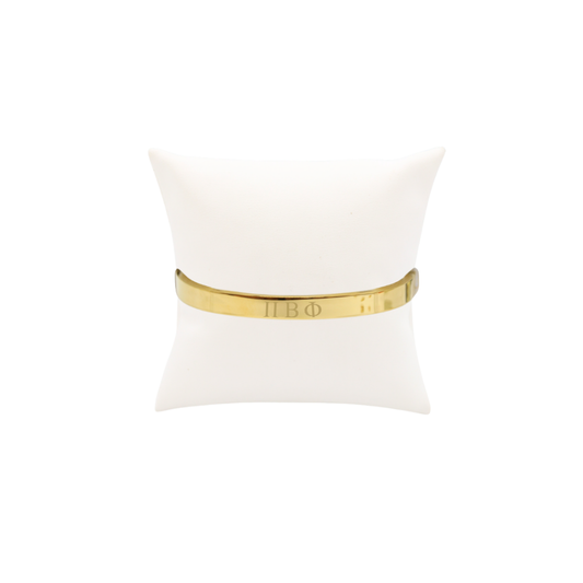 Pi Beta Phi gold bangle bracelet displayed on white pillow front view with horizontal greek letters