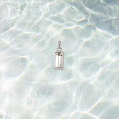 Silver rectangular clear crystal gemstone charm with a faceted baguette-cut stone on a shimmering light blue water background.
