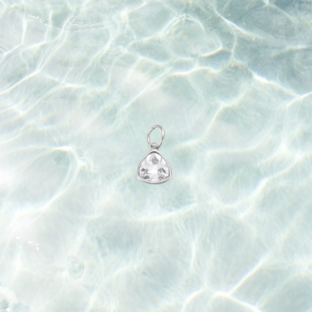 Silver clear triangle gemstone charm featuring a faceted crystal in a polished silver setting on a shimmering water background