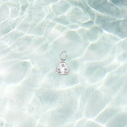 Silver clear triangle gemstone charm featuring a faceted crystal in a polished silver setting on a shimmering water background