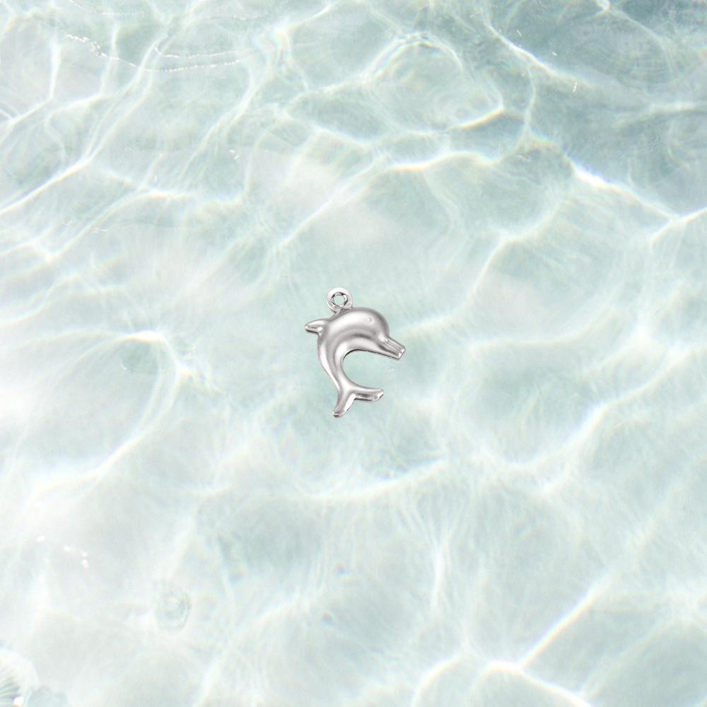 Silver dolphin charm on a shimmering water background, featuring a polished dolphin design with a pre-installed gold jump ring.