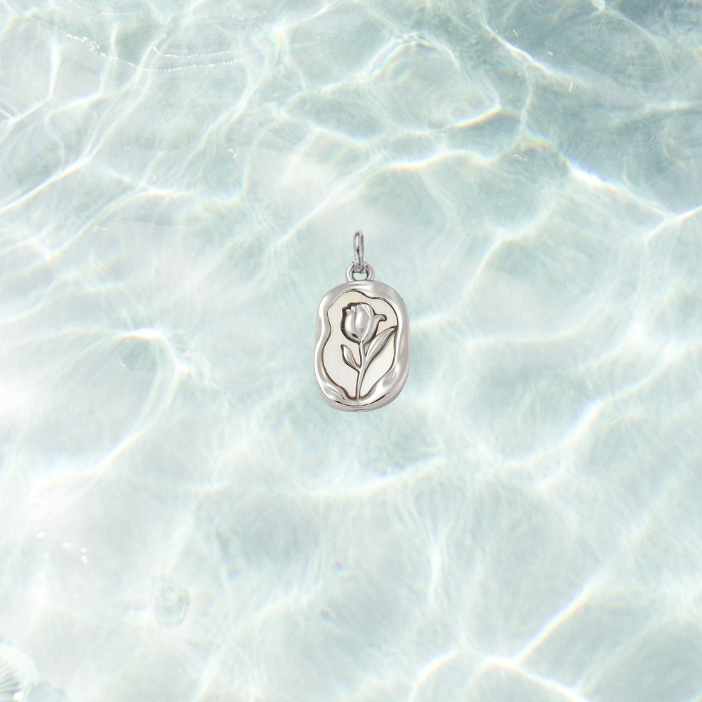 Silver embossed vintage rose charm featuring a raised floral design on an organic rectangular pendant, displayed on a shimmering light blue water background