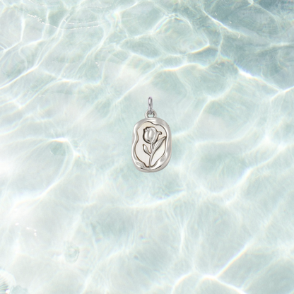 Silver embossed vintage rose charm featuring a raised floral design on an organic rectangular pendant, displayed on a shimmering light blue water background