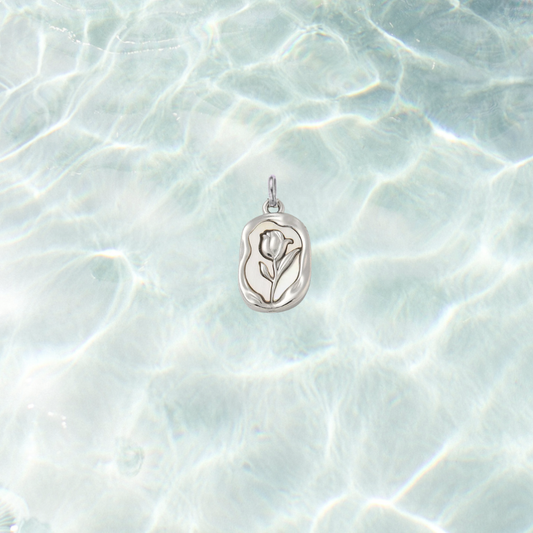 Silver embossed vintage rose charm featuring a raised floral design on an organic rectangular pendant, displayed on a shimmering light blue water background