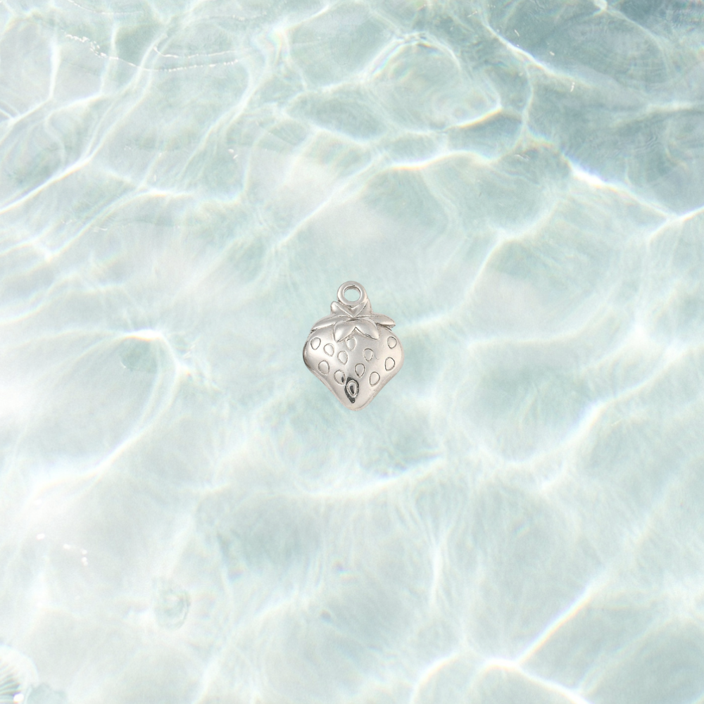 Silver strawberry charm with engraved seed details and leafy top on a shimmering water background.