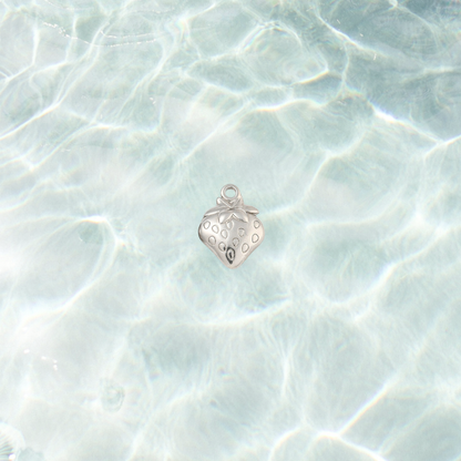 Silver strawberry charm with engraved seed details and leafy top on a shimmering water background.