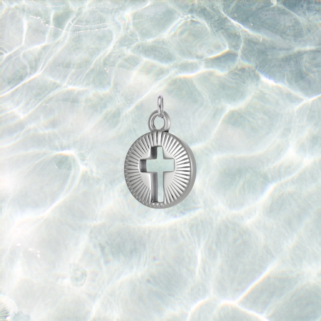 Silver Gleaming Center Cross charm featuring a cutout cross with engraved sunburst detailing, displayed on a shimmering light blue water background.