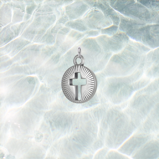 Silver Gleaming Center Cross charm featuring a cutout cross with engraved sunburst detailing, displayed on a shimmering light blue water background.