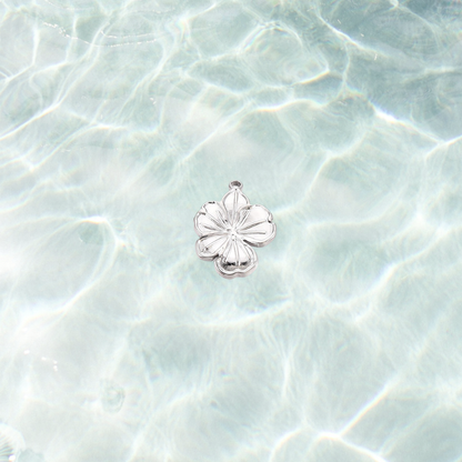 Silver hibiscus flower charm with detailed tropical petals displayed against a soft blue water-inspired background.