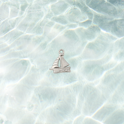 Silver nautical sailboat charm with engraved sail and wave details on a shimmering water background.