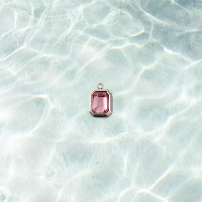 Silver rectangular charm featuring a faceted flamingo pink gemstone on a shimmering water background.