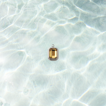 Silver rectangular charm featuring a faceted topaz gemstone on a shimmering water background.