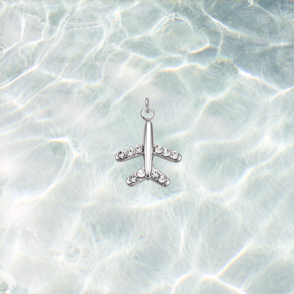 Silver waterproof airplane charm accented with rhinestones on the wings and tail, displayed on a shimmering light blue water background