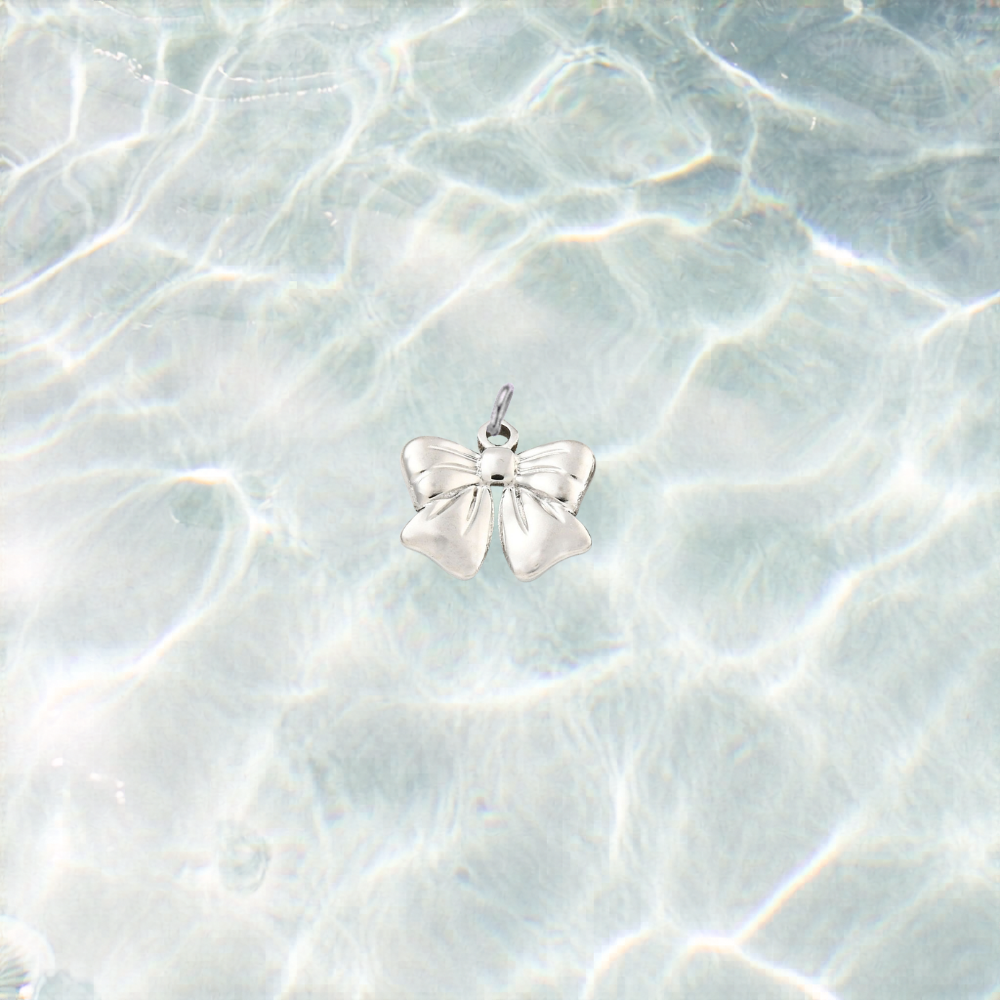 Silver waterproof bow charm with a polished finish on a shimmering light blue water background.