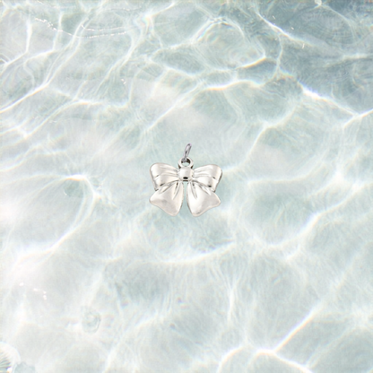 Silver waterproof bow charm with a polished finish on a shimmering light blue water background.