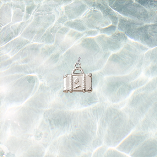 Silver waterproof suitcase charm with a polished finish on a shimmering light blue water background.