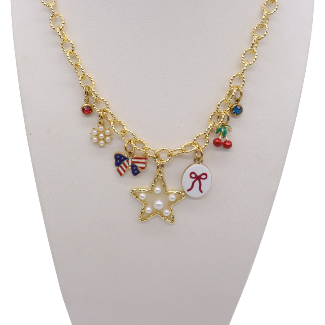 Gold charm necklace featuring a pearl star charm, patriotic bow charm, cherries, pearl cluster, bow illustration charm, and colorful crystal accents displayed on a white jewelry bust