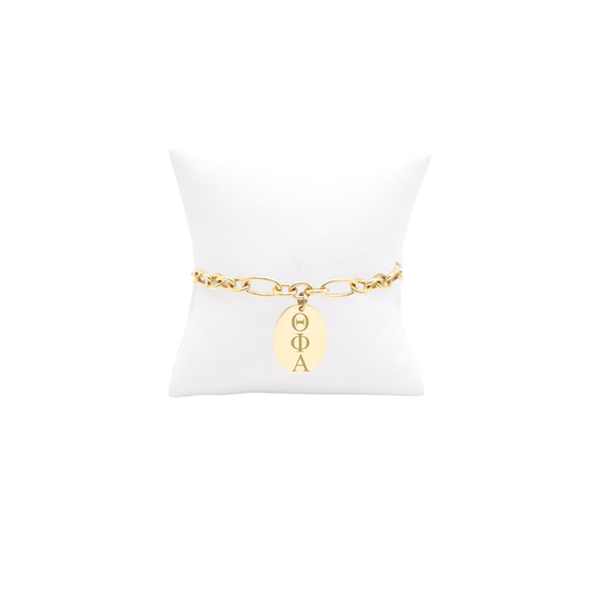 Theta Phi Alpha gold large link keepsake bracelet with large oval charm displayed on white pillow front view with horizontal greek letters