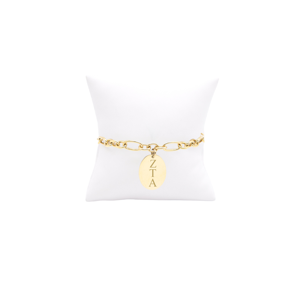 Zeta Tau Alpha gold large link Keepsake bracelet with large oval charm with vertical greek letters on white pillow front view.