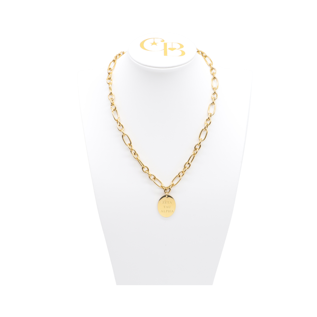 Zeta Tau Alpha gold large link Keepsake necklace with large oval charm with full sorority name on white pillow front view.